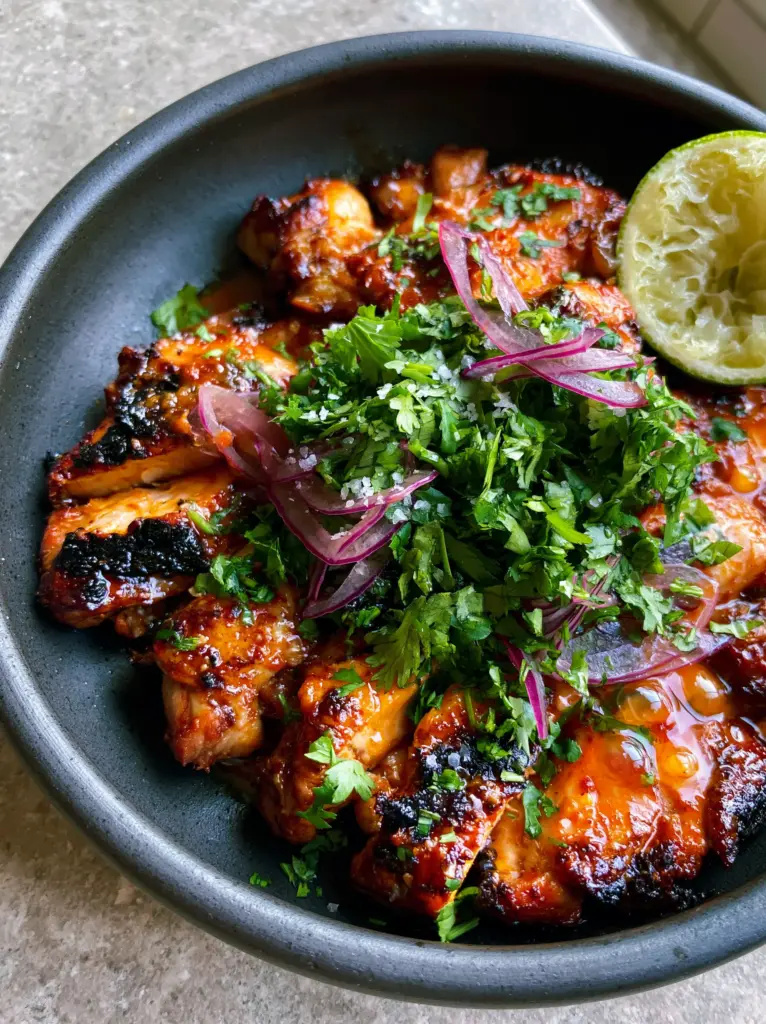 Grilled chicken thighs with a vibrant orange-red citrus glaze and translucent red onion slivers.