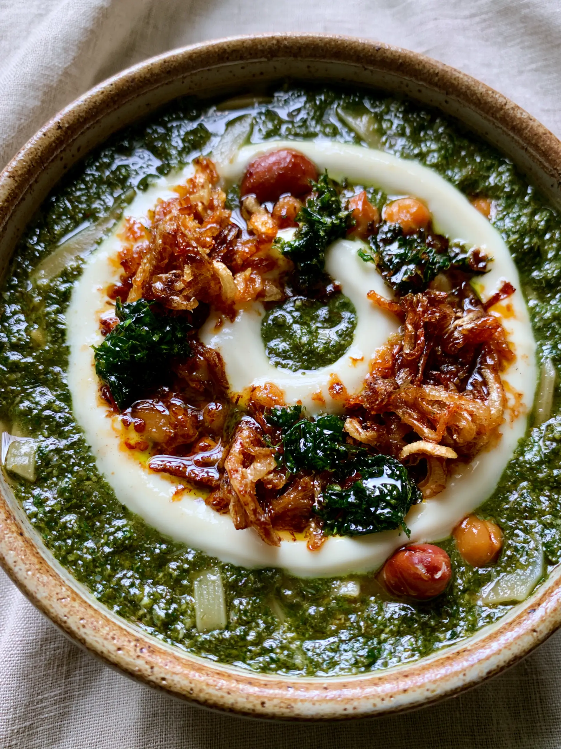A close-up view of a thick green herb broth with flat wheat noodles and golden onions. (Persian Soup Recipe)