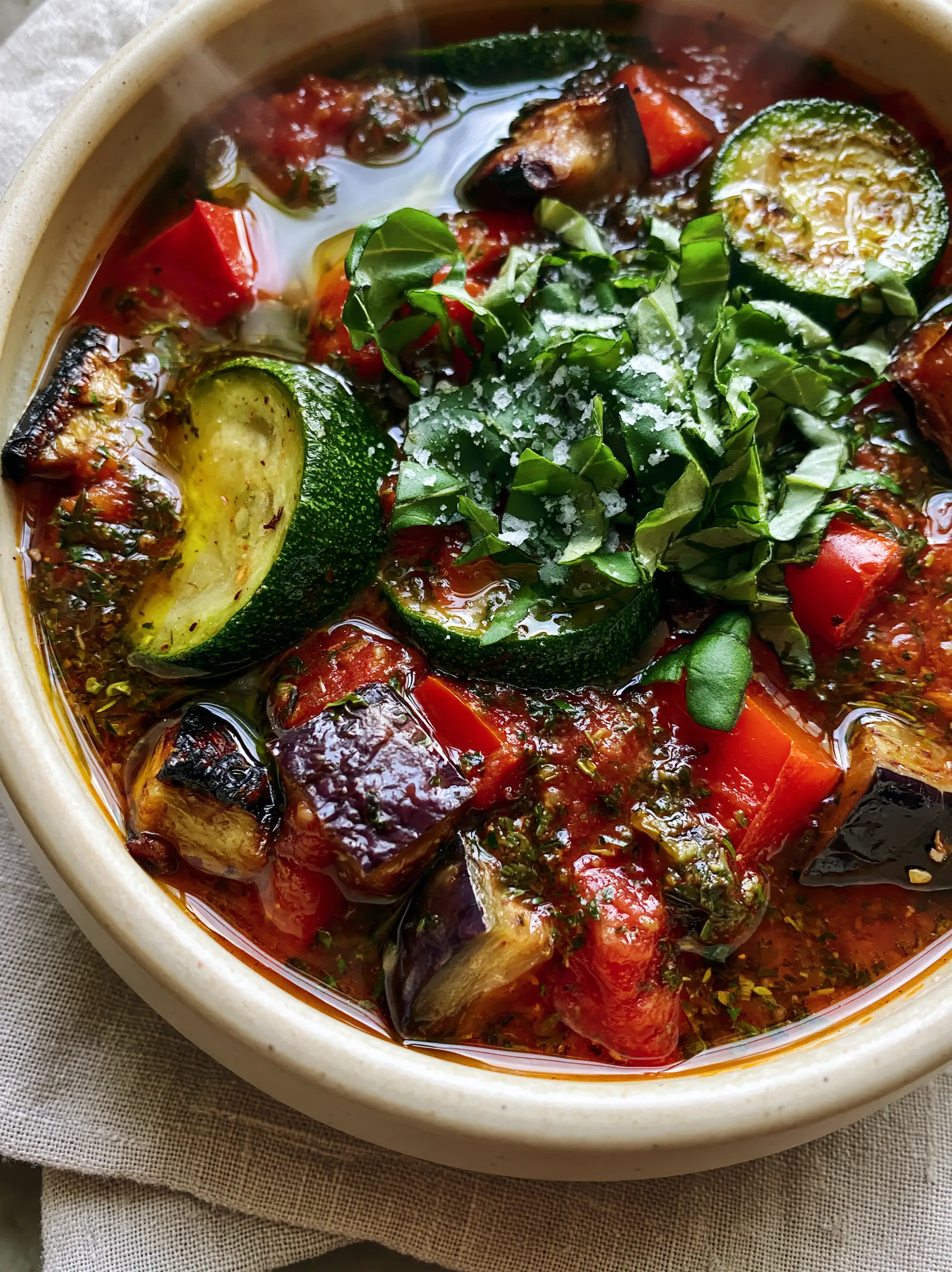 Top-down macro shot of ratatouille soup showing glossy olive oil drizzle and vibrant zucchini rounds. (ratatouille soup)