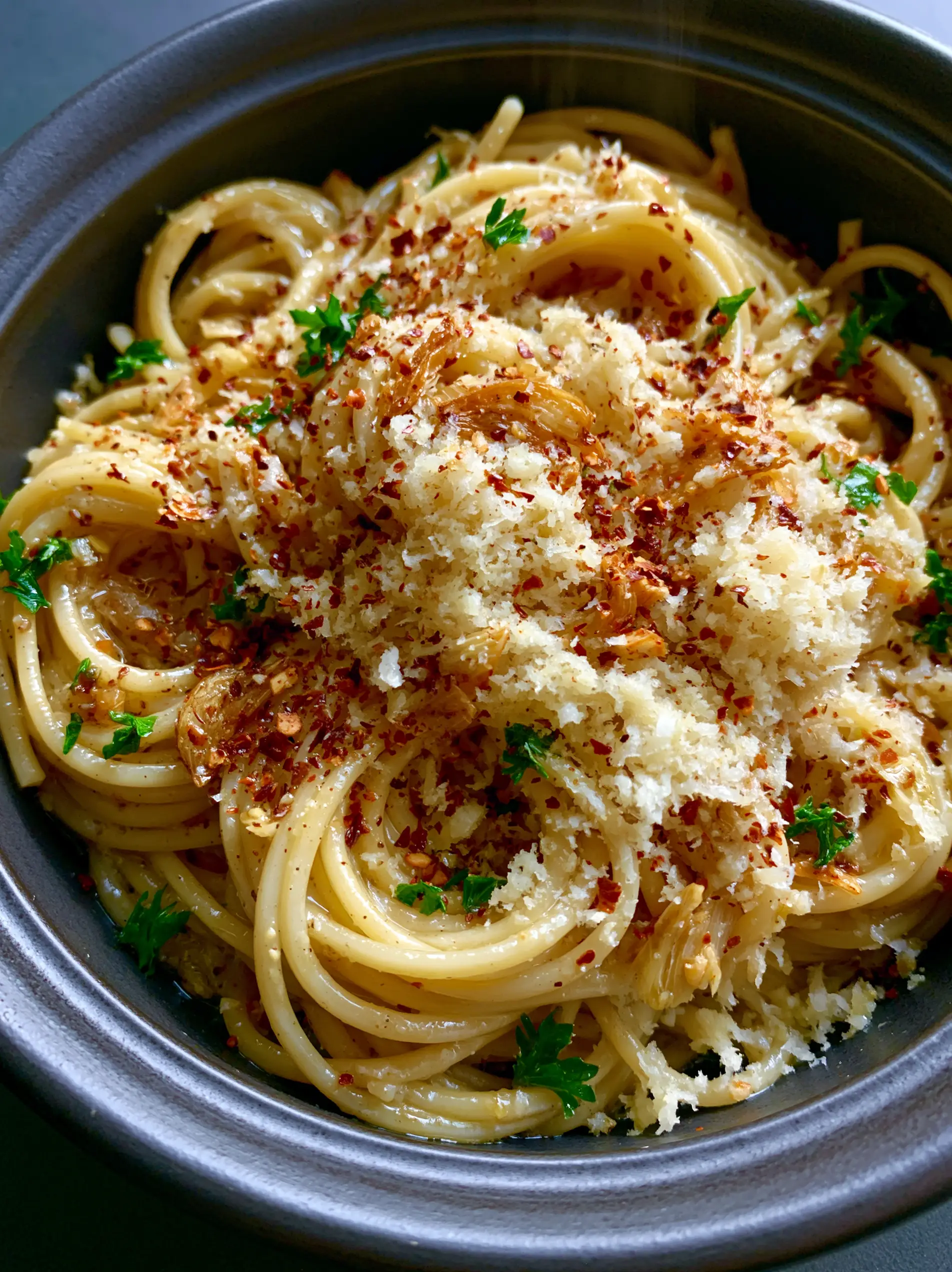 Top-down angled shot of glistening Garlic butter pasta in a charcoal bowl with steam rising. (Garlic butter pasta)