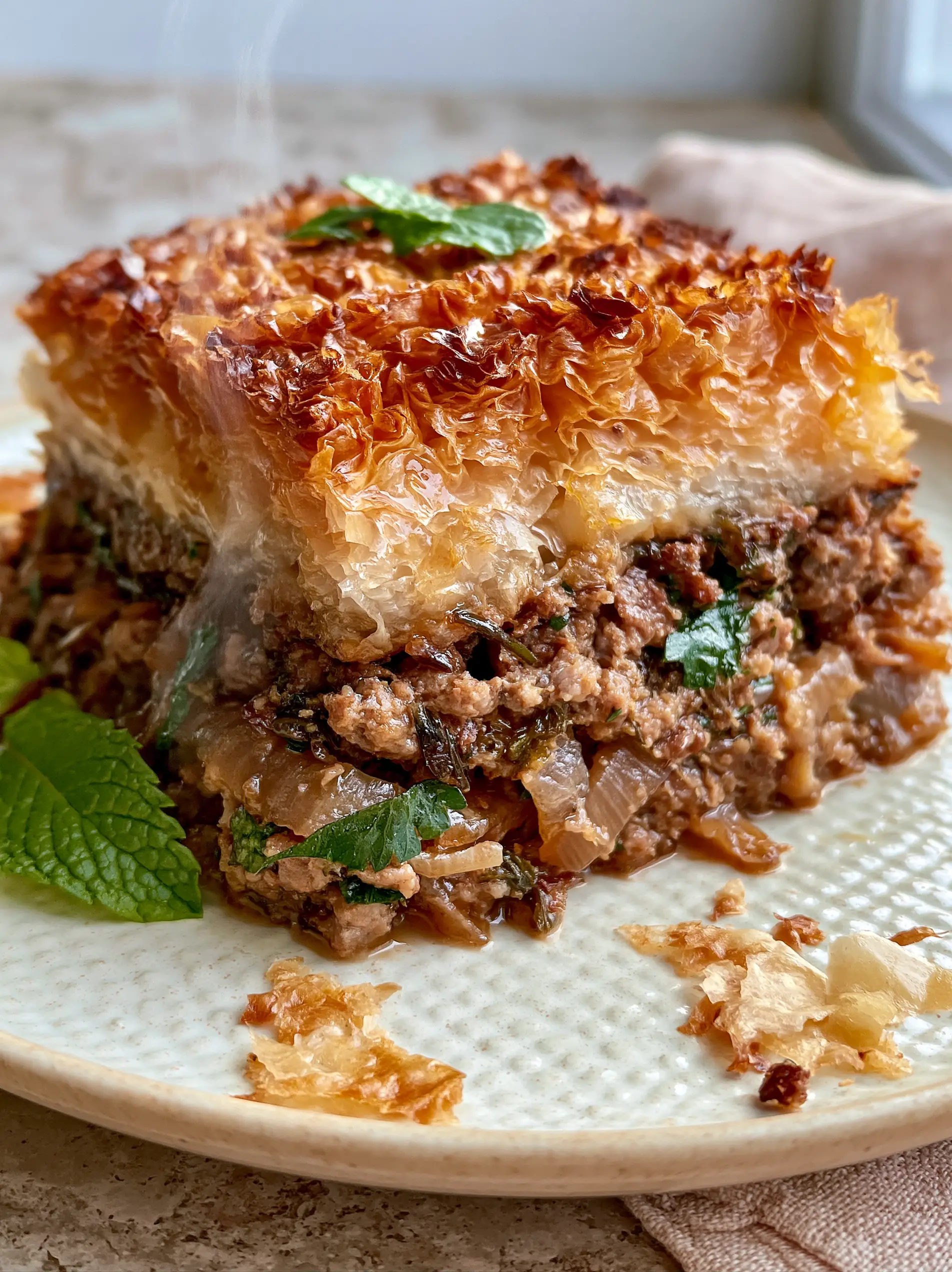 Close-up cross-section of a Greek Meat Pie square revealing steamed seasoned ground lamb and herbs beneath crisp pastry layers.