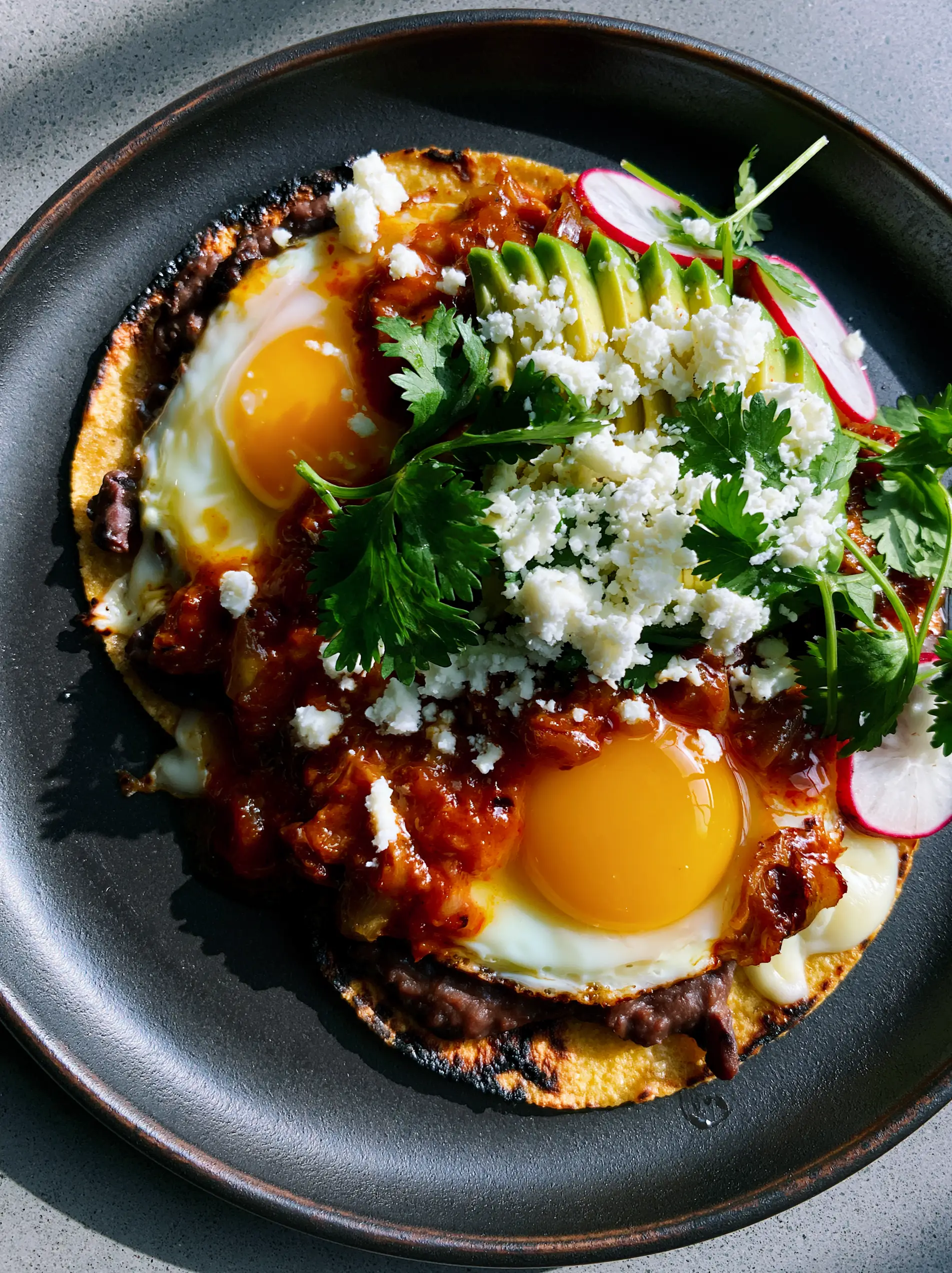 Close-up of sunny-side-up eggs with vibrant orange yolks on a bed of black beans and melted cheese for Huevos rancheros.
