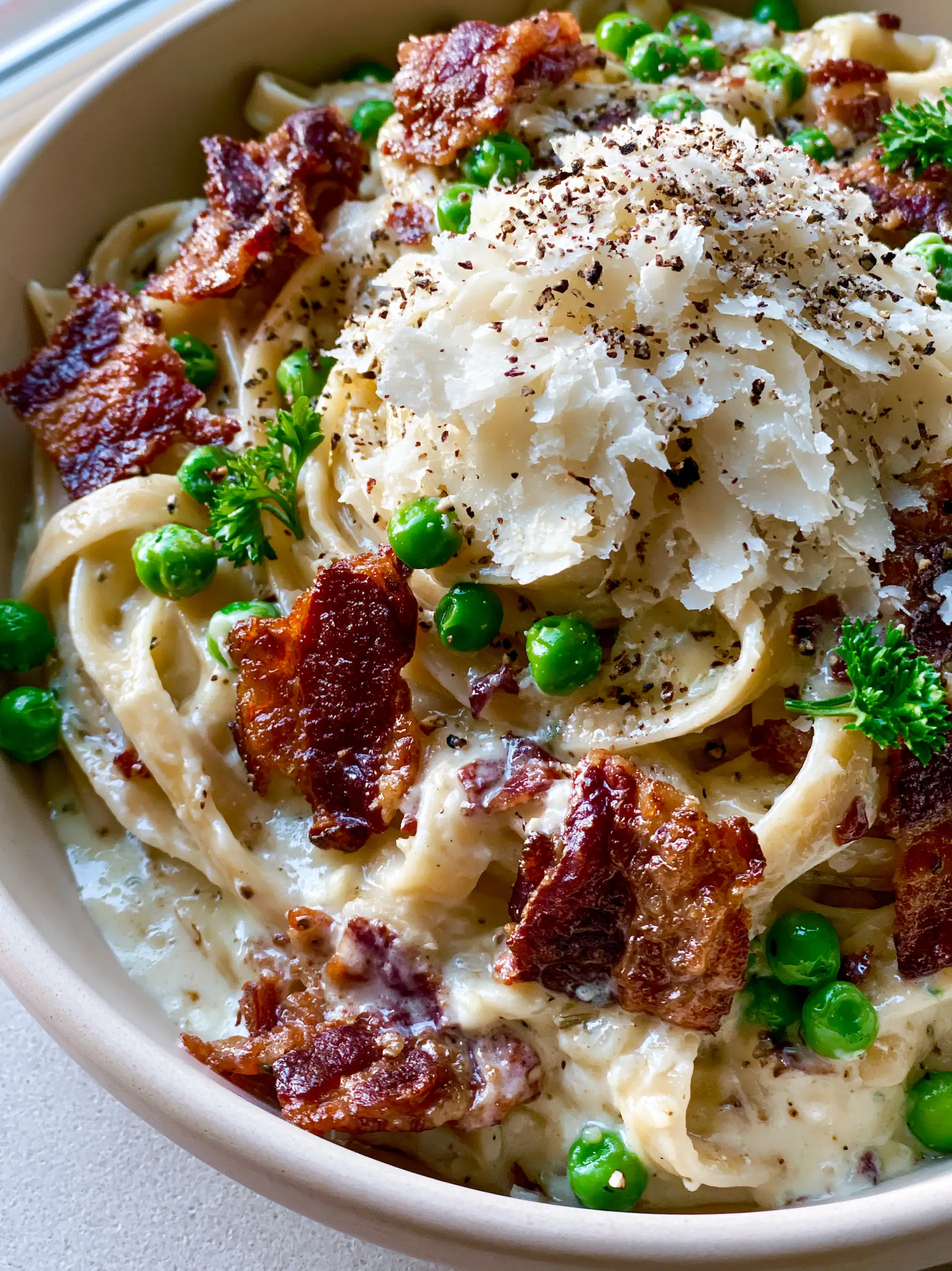 Close-up of al dente fettuccine coated in garlic parmesan sauce with mahogany bacon and green peas.