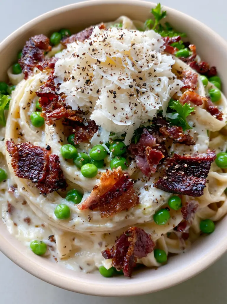 Extreme top-down view of Bacon and Pea Pasta showing fluffy microplaned parmesan and coarse black pepper.