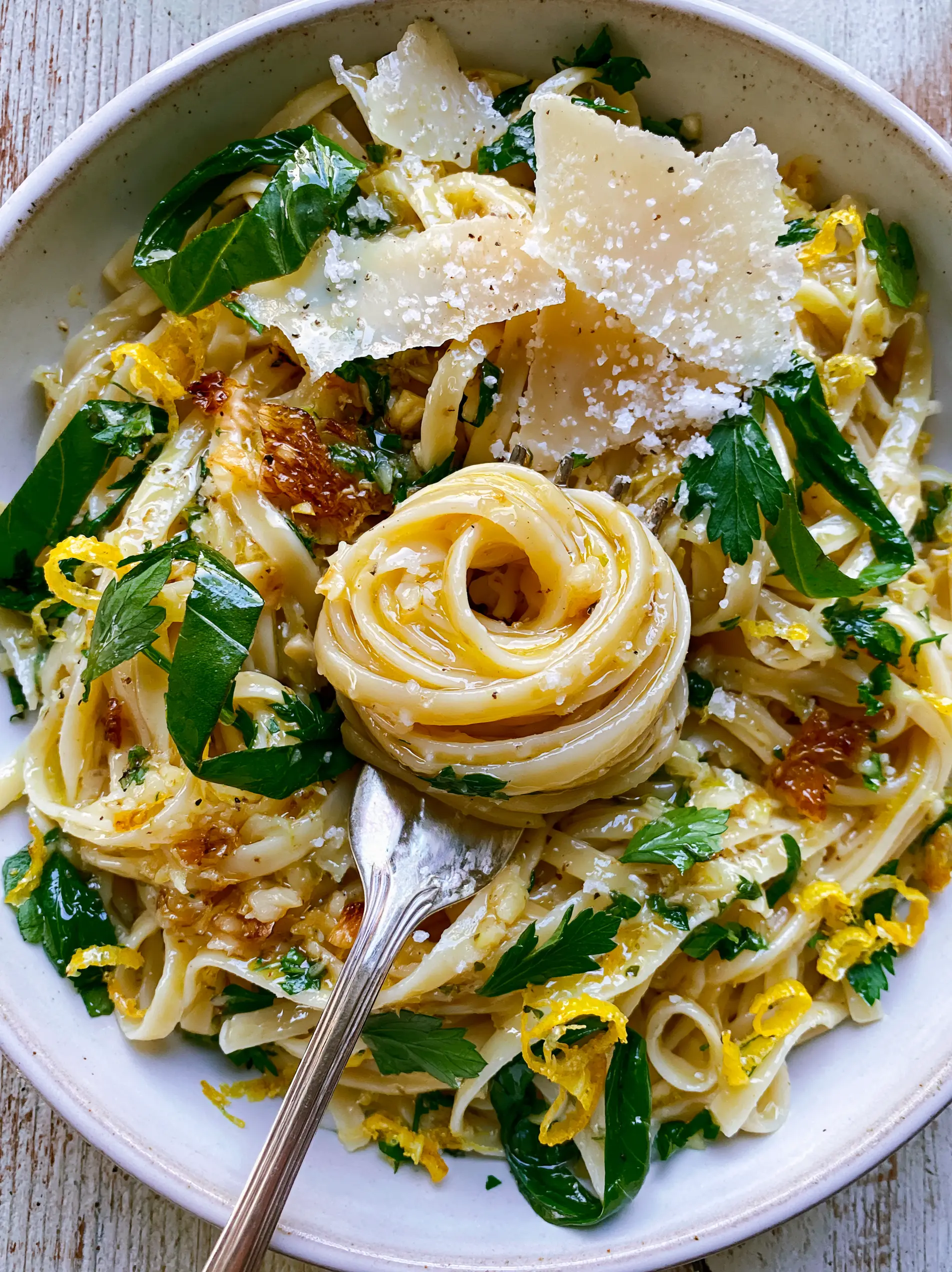 Close-up of glistening linguine pasta coated in a golden-yellow lemon emulsion with toasted garlic and green basil ribbons. (Summer Pasta Recipe)