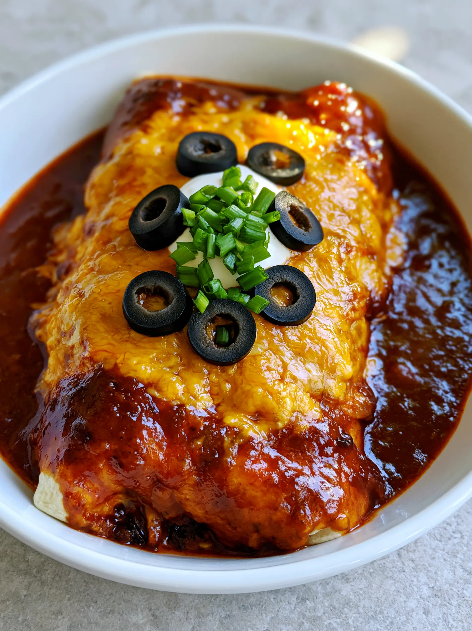 Overhead view of a saucy Enchirito topped with melted yellow cheddar, black olives, and green onions. (Enchirito)
