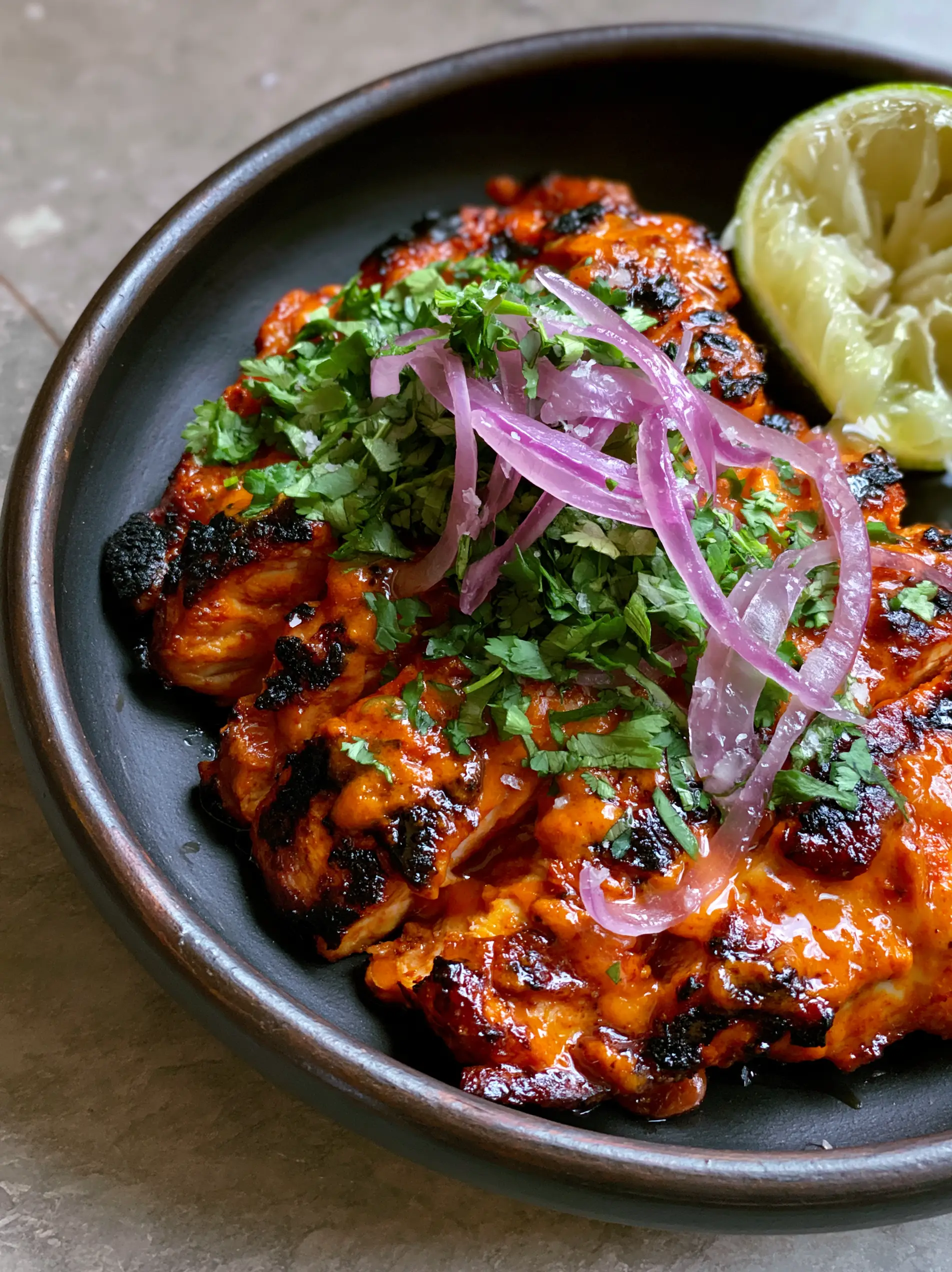 Macro shot of sliced grilled chicken dripping with orange-red Mexican chicken marinade and lime droplets.